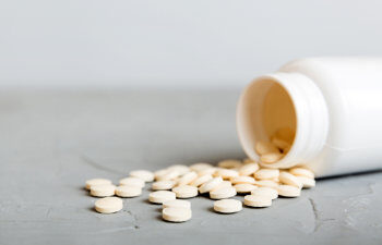 medicine bottle and white pills spilled on a light background