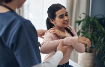 Woman, doctor and appointment with shoulder pain, medical and patient conversation for health care concern. Clinic, muscle tension and talking with medic employee, injury and professional help
