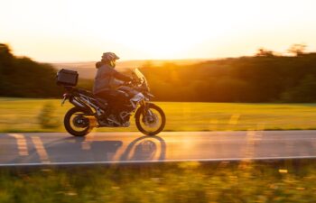 Driver riding motorcycle on empty road during sunset